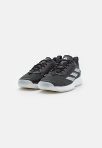 Black athletic shoes with a textured fabric upper, featuring three white stripes, a white sole, and a patterned rubber outsole.