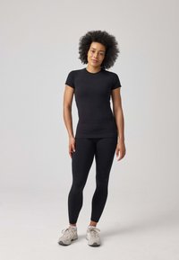 Zwarte, aansluitende sporttop en leggings gemaakt van rekbaar materiaal, gecombineerd met lichtgrijze sneakers. Eenvoudig ontwerp zonder patronen.