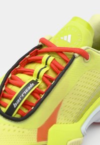 Neon yellow athletic shoe features red laces, black and yellow accents, and a textured pattern on the side. "barricade" logo is visible.