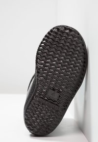 Suela de zapato de goma negra con patrón de zigzag texturizado, que presenta un logotipo cuadrado y detalles de tamaño grabados en el costado.