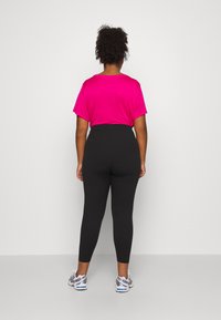 Fuchsia kortærmet top og højtaljede sorte leggings, der har en glat tekstur og tætsiddende design, parret med grå træningssko.