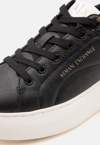 Μαύρο sneaker από δέρμα με υφή, μαύρα κορδόνια, λευκή σόλα και χρυσό λογότυπο Armani Exchange στο πλάι.