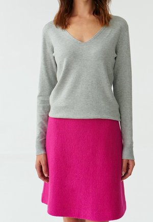 Maglione grigio chiaro con scollo a V e maniche lunghe abbinato a una gonna in feltro rosa vivace, lunga fino al ginocchio. Texture morbide e colori a contrasto.