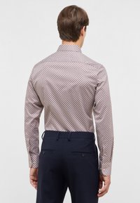 Camicia a maniche lunghe con un motivo geometrico in rosso e bianco, in cotone, abbinata a pantaloni blu navy con tasche posteriori.