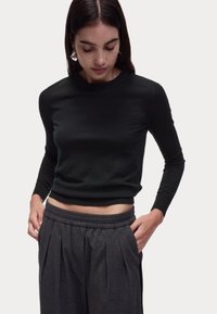 Maglione aderente nero realizzato in tessuto morbido, con maniche lunghe e scollo a girocollo, abbinato a pantaloni grigi a vita alta con pieghe.