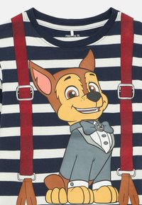 Gestreiftes T-Shirt in Marineblau und Weiß mit einem cartoonhaften Hund im Smoking und roten Hosenträgern. Das Design des Hundes umfasst große, ausdrucksvolle Augen und eine Fliege.