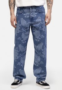 Blue denim jeans with a floral pattern in light blue. Straight cut legs and a mid-rise waist, paired with black sneakers.