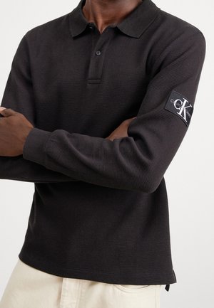 Zwarte longsleeve poloshirt van textiel met een structuur, voorzien van een drieknoopsluiting en een logopatch op de linker mouw.