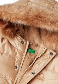 Tan zateplená bunda s kapucí lemovanou umělou kožešinou, s patentním zapínáním a texturovaným interiérem. Obsahuje zelenou nálepku s označením "Vybrané barvy".