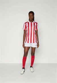 Červený a bílý vodorovně pruhovaný fotbalový dres s krátkým rukávem a logem, spárovaný s bílými šortkami a červenými podkolenkami; černé kopačky.