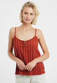 Top senza maniche color ruggine con sottili spalline, caratterizzato da strisce verticali bianche e un dettaglio con lacci sul collo. Tessuto leggero.