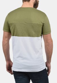 Korte mouwen t-shirt met een olijfgroene bovenkant met een gestructureerde textuur en een witte onderkant, gemaakt van een zachte stof.