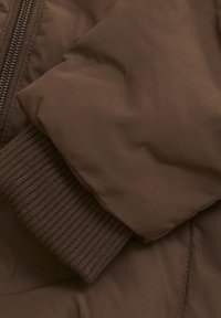 Brown puffer jacket sleeve featuring a smooth, matte texture with a ribbed brown knit cuff. Zipper visible along the seam.