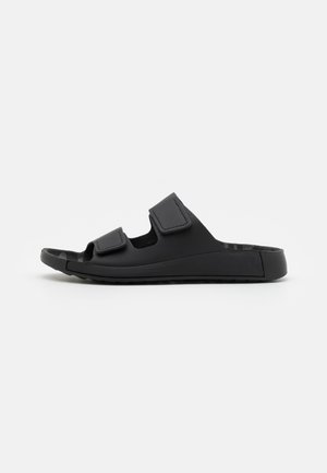 Zwarte instap-sandalen met dubbele klittenbandbandjes, gemaakt van glad materiaal, met een gestructureerde binnenzool en een platte, duurzame buitenzool.