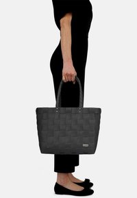 Schwarze geflochtene Tragetasche mit zwei stabilen Griffen, rechteckiger Form, glatter Textur und einem kleinen Logo-Tag auf einer Seite.