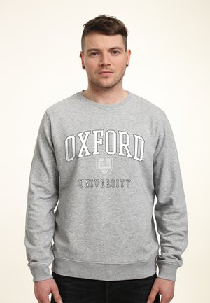 Felpa grigia con maniche lunghe, collo a giro, con la scritta "OXFORD UNIVERSITY" in grassetto, nero, sul petto. Tessuto morbido.