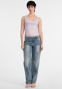 Canotta aderente lilla con design grafico, abbinata a jeans dritti azzurri chiari e ciabatte bianche; look minimalista e casual.