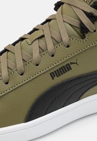 Sněrky z olivově zelené kůže s béžovými tkaničkami, černými akcenty a bílou podrážkou. Výrazné logo Puma. Texturovaný povrch.