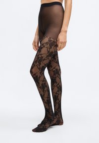 Μαύροι καλσόν από δαντέλα με λουλουδάτα μοτίβα, ημιδιάφανο υλικό και ψηλή μέση. Σχεδίαση με ανοιχτά δάχτυλα και ομαλή υφή.