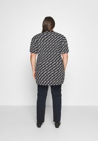 Svart t-shirt med vitt upprepande textmönster, kort ärm och lös passform. Matchad med marinblå byxor och svarta skor.