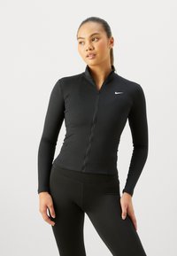 Musta vetoketjullinen urheilu takki pitkähihaisilla ja istuvalla designilla. Varustettu pystykauluksella ja pienellä valkoisella Nike-logolla rinnassa.