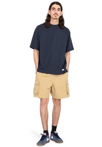 Marineblå kortærmet raglan t-shirt parret med khaki cargo shorts. Struktureret stof, sidelommer i shortsene og kontrastfarvet fodtøj.
