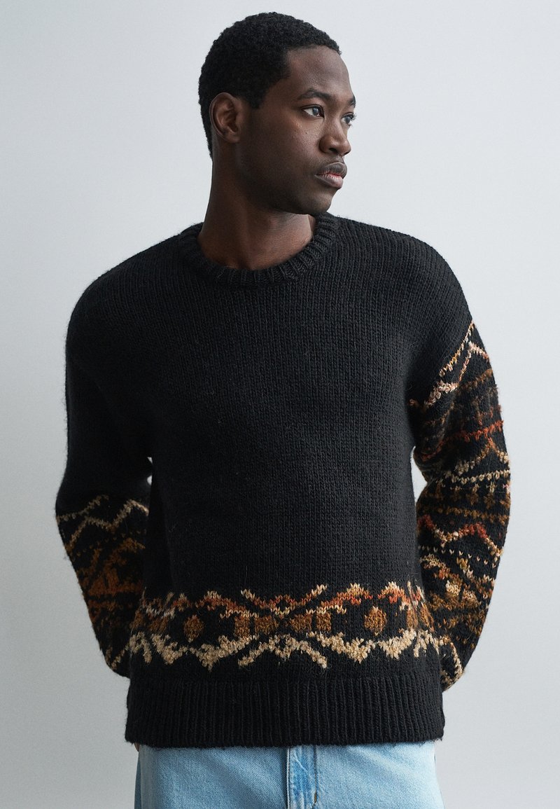 Fekete kötött pulóver texturált anyagból, színes geometrikus mintával a karokon és az alsó szegélyen. Kerek nyakú.