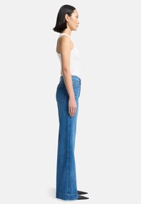 Hoch taillierte, ausgestellte Jeans aus blauem Denim. Verfügt über ein klassisches Fünf-Taschen-Design, gerades Bein und ausgefranstes Saum-Detail.