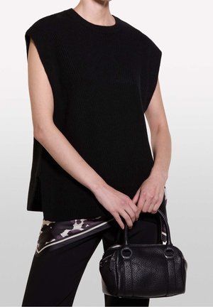 Person iført en ærmeløs sort sweater og et mønstret tørklæde, der holder en lille, tekstureret sort læderhåndtaske med to håndtag.