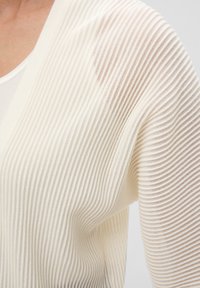 Lichte, ribgebreide cardigan in off-white, met een zachte textuur en een open voorkant. Versterkt met doorschijnende stof langs de schouders.