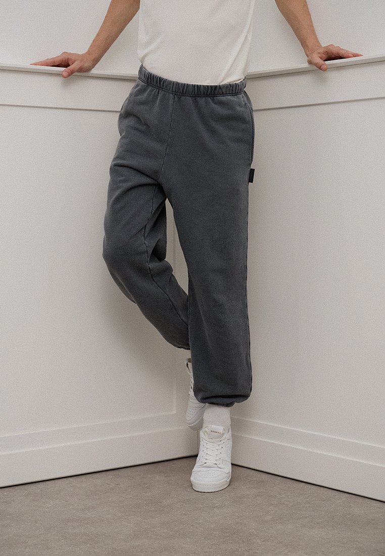 Pantalones de chándal grises con cinta elástica en la cintura y bolsillos laterales, con un corte relajado y tobillos ajustados, combinados con zapatillas blancas.