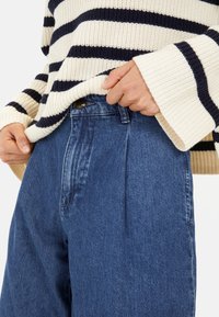 Chunky gebreide crème trui met marineblauwe strepen, gecombineerd met hoge blauwe denim broek met knoopsluiting en voorplooien.