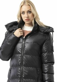 Schwarze, wattierte Jacke mit Reißverschluss, verstellbarer Kapuze und Seitentaschen. Sie zeichnet sich durch eine glänzende Oberfläche und ein gesteppte Design zur Isolierung aus.