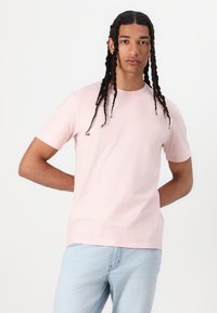 Helles rosa Baumwoll-T-Shirt mit rundem Halsausschnitt und kurzen Ärmeln, das über eine glatte Textur und eine normale Passform verfügt. Lässiges Design ohne Muster.