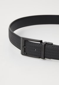 Cinturón de cuero negro con un patrón texturizado, que presenta una hebilla metálica rectangular y múltiples agujeros de ajuste para el tamaño.