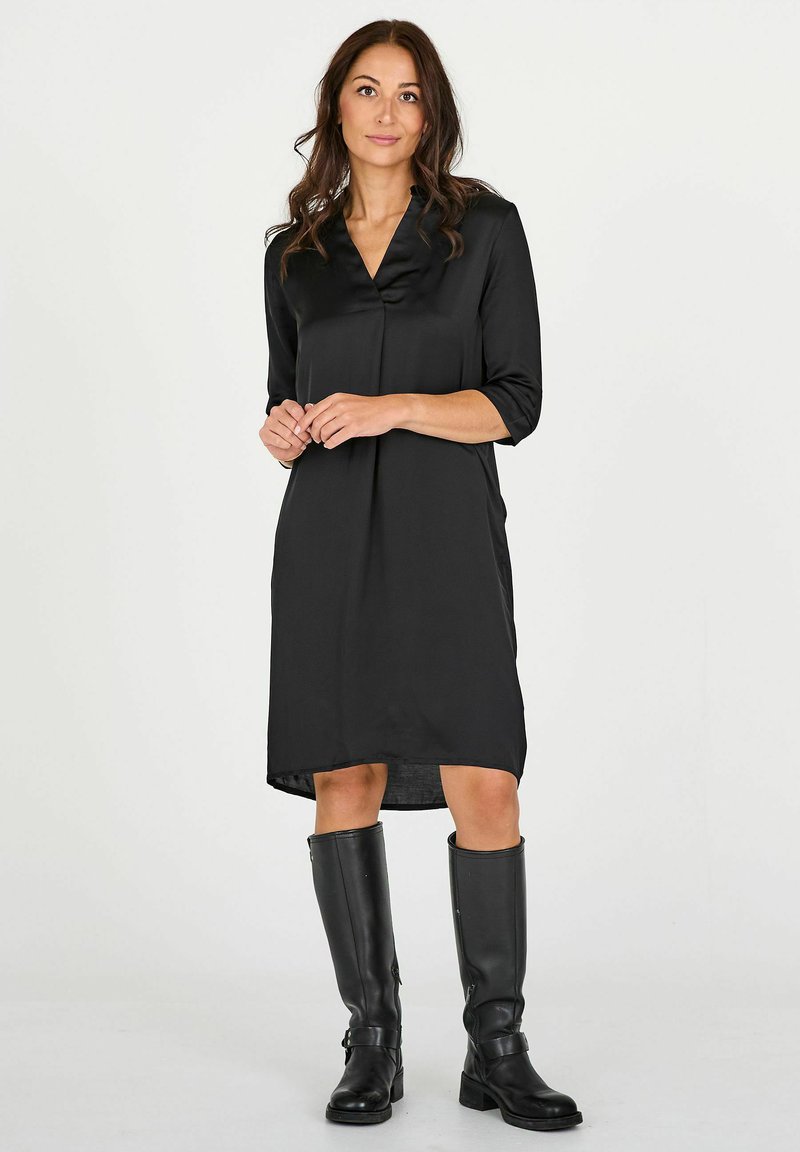Vestido de satén negro con escote en V, mangas tres cuartos y un corte relajado. Combina con botas de cuero negro hasta la rodilla.