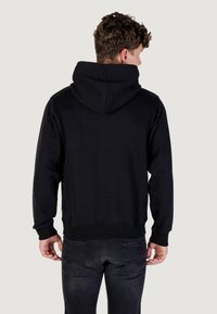 Sudadera negra con una gran capucha, puños y cintura acanalados. Textura suave, diseño minimalista y sin patrones ni logotipos visibles.