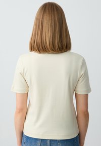 Crème korte mouwen t-shirt van zachte stof, met een ronde halslijn en een getailleerde pasvorm, gecombineerd met hoge taille blauwe jeans.