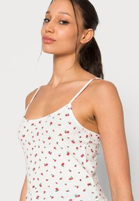 Top de alças branco com padrão de cerejas vermelhas, alças finas e silhueta ajustada. Apresenta um decote em forma de scoop e tecido leve.