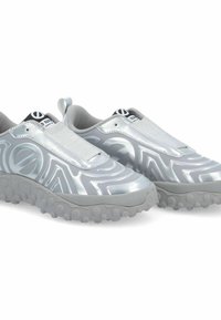 Silberne Slip-On-Sportschuhe mit einer strukturierten, glänzenden Oberseite und grauen Gummisohlen, die kleine Vorsprünge für besseren Halt aufweisen.