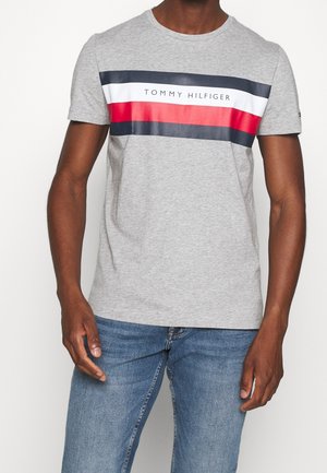 Graues Baumwoll-T-Shirt mit einem horizontalen Streifenmuster in Marineblau, Rot und Weiß, mit dem Logo "TOMMY HILFIGER" in der Mitte aufgedruckt.