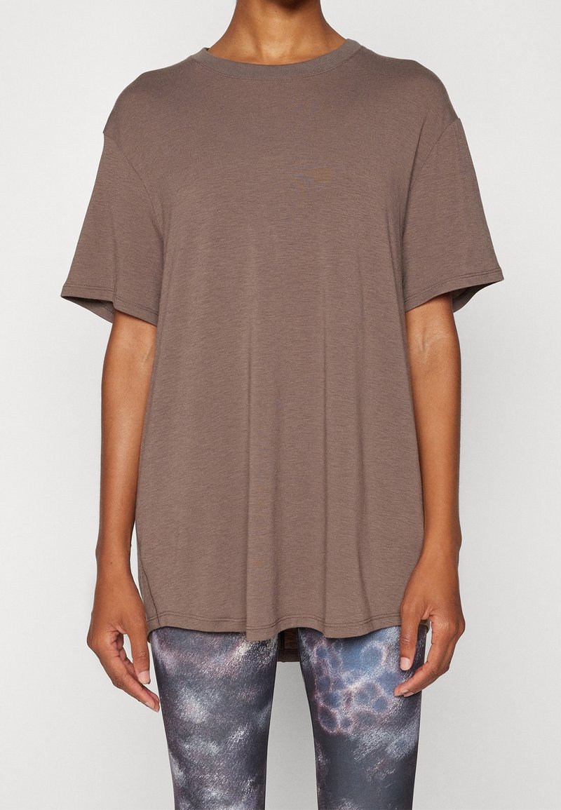 Camiseta marrón de manga corta con un corte relajado y cuello redondo, combinada con leggings estampados en tonos de gris y azul.