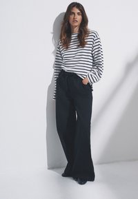 Pantalones anchos negros combinados con una camisa de manga larga blanca con rayas azul marino. El conjunto presenta cortes relajados y elementos de diseño sencillos.