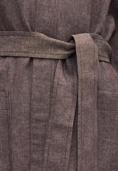 Κοντινό πλάνο ενός καφέ υφασμάτινου ζώνης με υφή που είναι δεμένη γύρω από τη μέση, εμφανίζοντας λεπτομερή ραφές και μια τσέπη στο ρούχο.