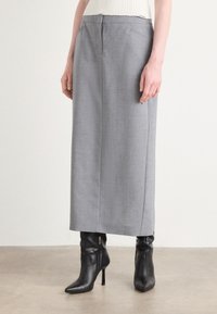 Grijze wijde broek van een gladde, lichte stof. Voorzien van steekzakken en een ritssluiting. Gemaakt in combinatie met zwarte puntige enkellaarsjes.
