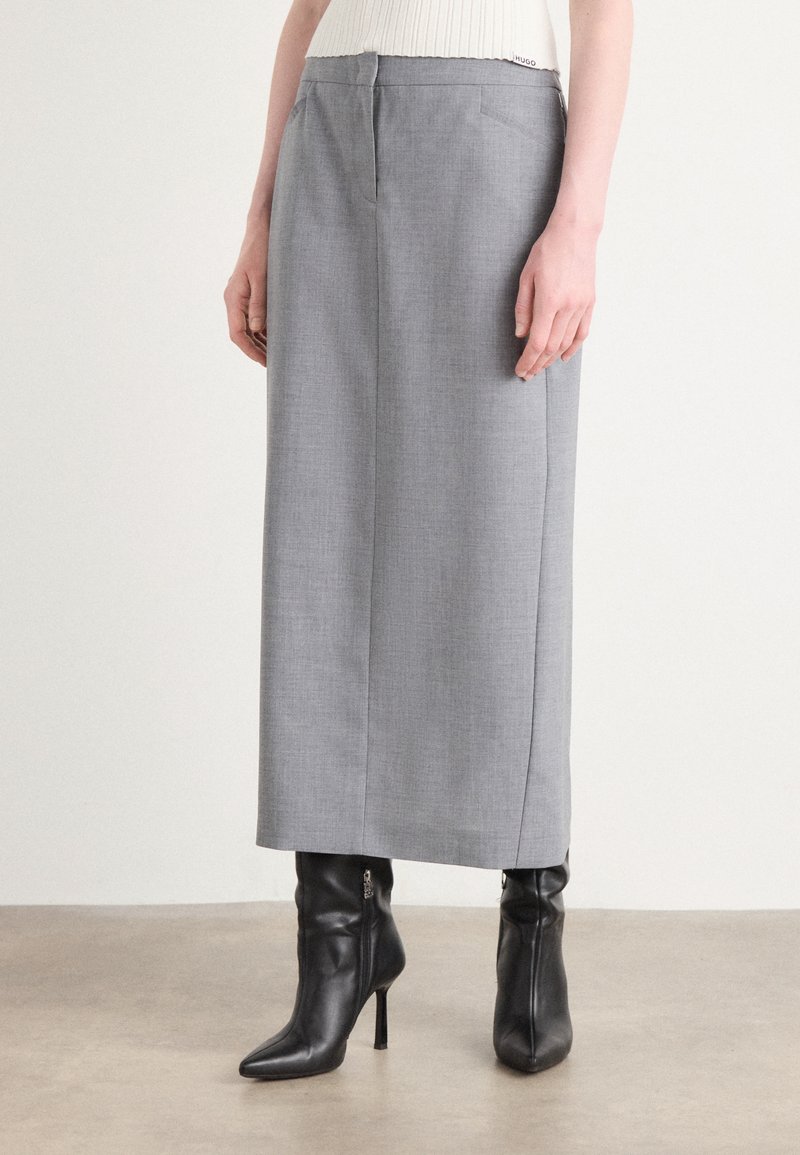 Grijze wijde broek van een gladde, lichte stof. Voorzien van steekzakken en een ritssluiting. Gemaakt in combinatie met zwarte puntige enkellaarsjes.