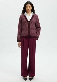 Burgundowa dziergana kardigan z dekoltem w serek, prążkowaną teksturą i zapięciem na guziki, w połączeniu z wysokimi śliwkowymi spodniami i czarnymi szpilkami.
