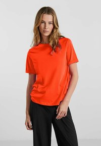 Orange kortærmet t-shirt i et blødt, glat stof. Klassisk crew neck-design med opkrøllede ærmer og en afslappet pasform.