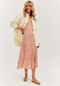 Maxi šaty v bielej farbe s korálovým vzorom pripomínajúcim koralový útes, so stranovým rozparkom. Skombinované s oversize krémovou košeľou na gombíky a sandálmi na šnúrky.