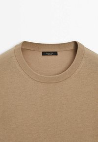 Pull en maille beige à col rond avec col côtelé et étiquette noire cousue à l'intérieur du col indiquant « Massimo Dutti Made in China ».